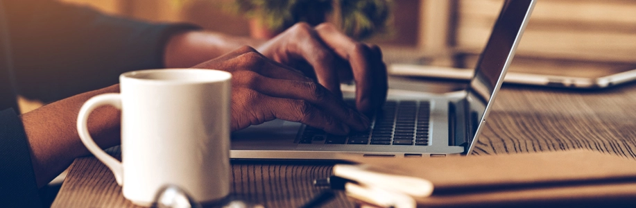 hands type on laptop next to white coffee mug